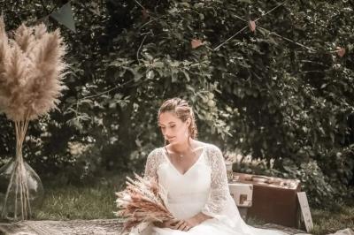 Une femme en robe de mariée est assise sur un tapis dans un jardin, tenant un bouquet de fleurs séchées.