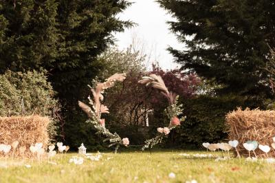 Une femme en robe de mariée est assise sur un tapis dans un jardin, tenant un bouquet de fleurs séchées.