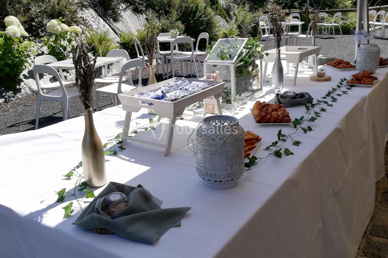 Table décorée pour un événement en extérieur, avec nappes blanches, lanternes, fleurs séchées et guirlandes lumineuses.