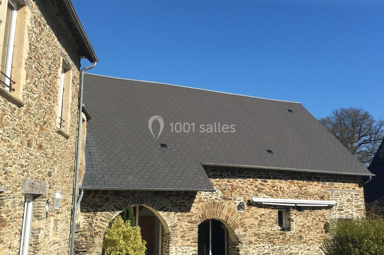 Bâtiment en pierre avec toit en ardoise sous un ciel bleu, comprenant des arches et des fenêtres.