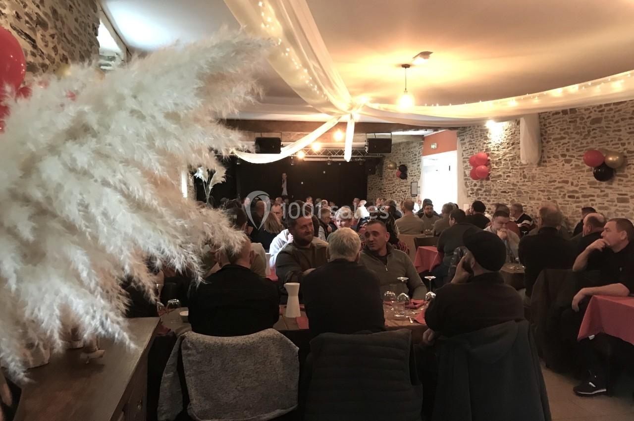 Salle décorée avec des guirlandes lumineuses, remplie de convives assis à des tables lors d'un événement festif.