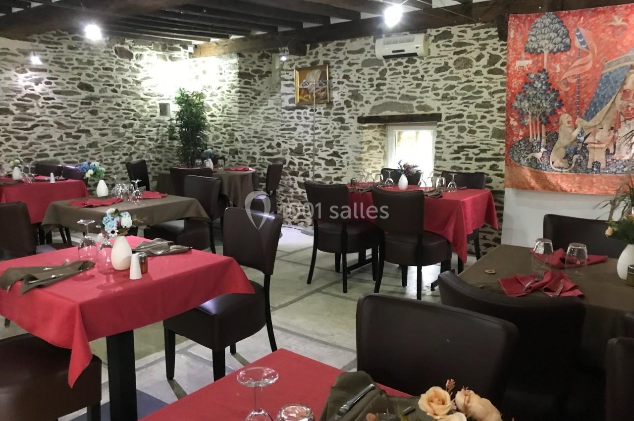 Salle de restaurant avec murs en pierre, tables dressées avec nappes rouges et brunes, décor rustique et chaleureux.