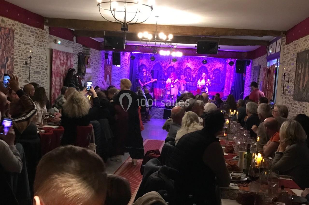 Salle de restaurant avec des convives assistant à un concert sur une scène éclairée, ambiance chaleureuse et festive.