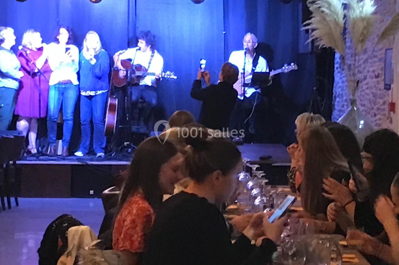 Des personnes dînent à des tables tandis qu'un groupe joue de la musique sur une scène éclairée.