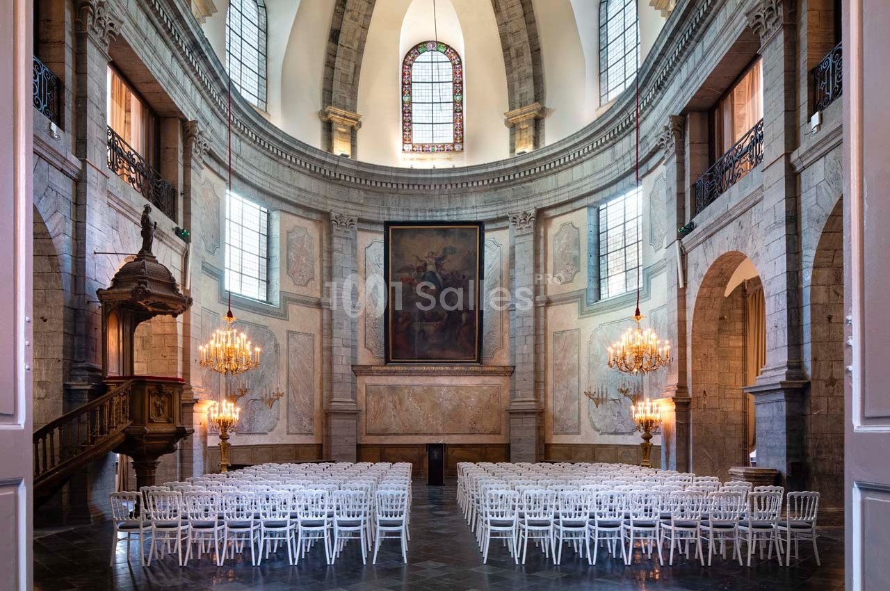Intérieur d'une église avec des rangées de chaises blanches, un plafond voûté et des lustres suspendus.