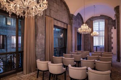 Chambre élégante avec lit double, fauteuil, rideaux beiges, tableaux encadrés et lumière naturelle entrant par une grande…