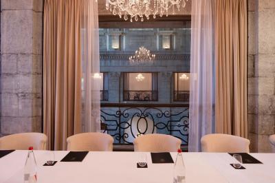 Chambre élégante avec lit double, fauteuil, rideaux beiges, tableaux encadrés et lumière naturelle entrant par une grande…