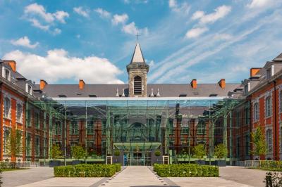 Chambre élégante avec lit double, fauteuil, rideaux beiges, tableaux encadrés et lumière naturelle entrant par une grande…