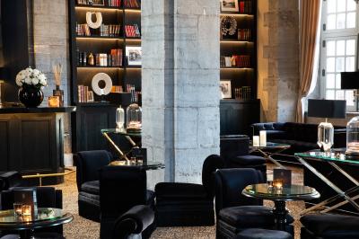 Chambre élégante avec lit double, fauteuil, rideaux beiges, tableaux encadrés et lumière naturelle entrant par une grande…