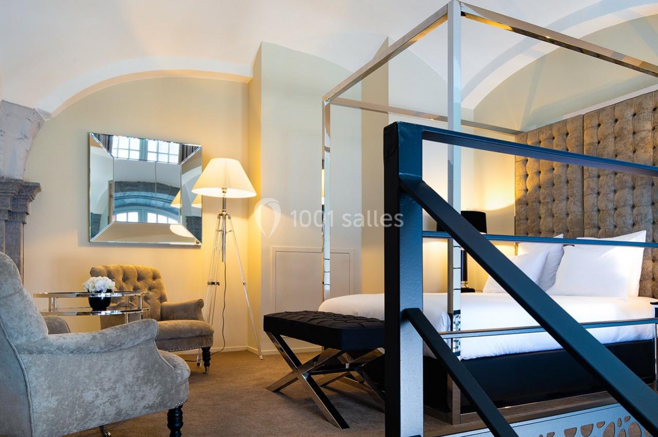 Chambre lumineuse avec lit à baldaquin, fauteuil, table en verre, miroir mural et lampadaire moderne.