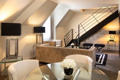 Chambre élégante avec lit double, fauteuil, rideaux beiges, tableaux encadrés et lumière naturelle entrant par une grande…