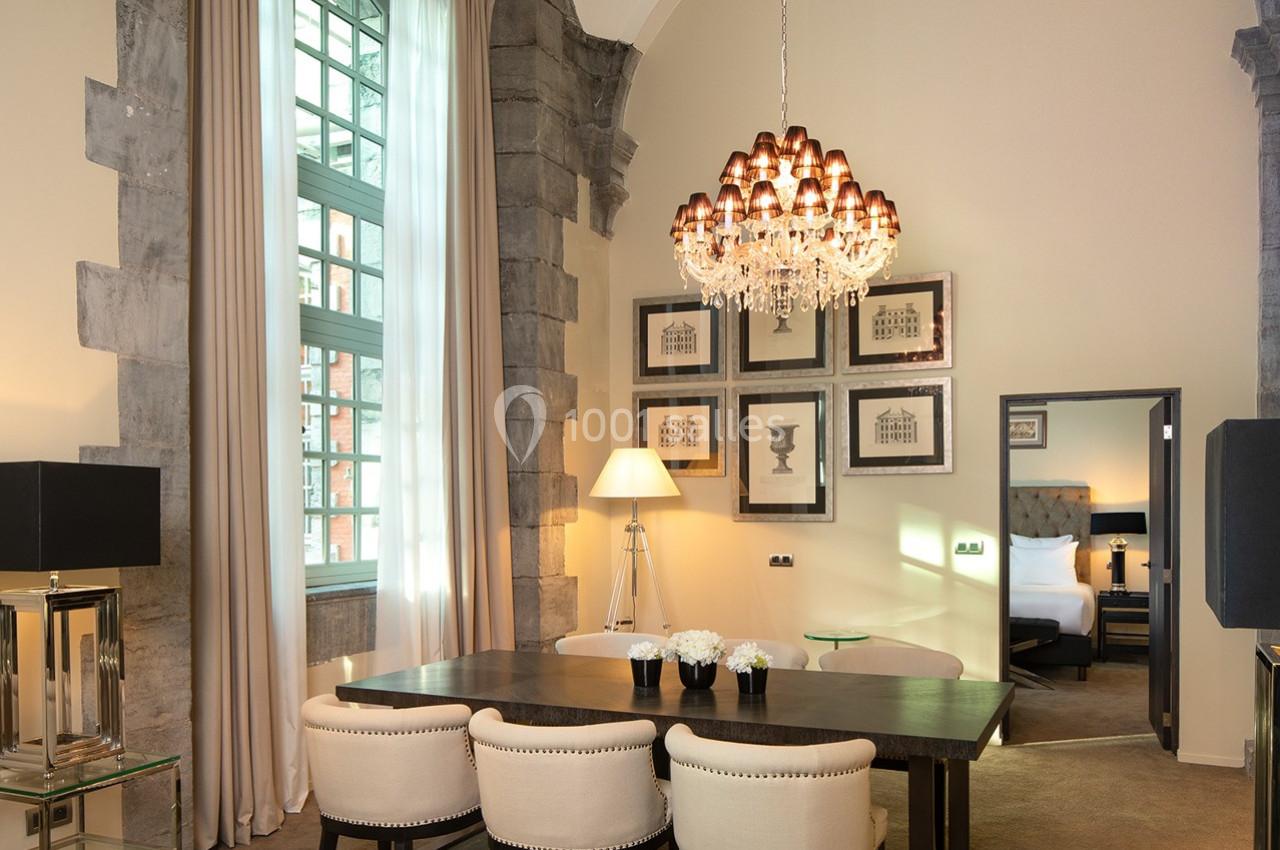 Salle à manger élégante avec table en bois, chaises rembourrées, lustre en cristal et vue sur une chambre adjacente.