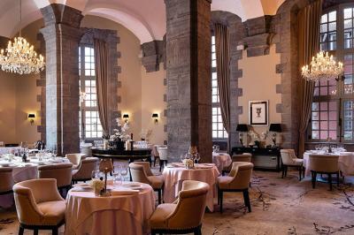 Chambre élégante avec lit double, fauteuil, rideaux beiges, tableaux encadrés et lumière naturelle entrant par une grande…