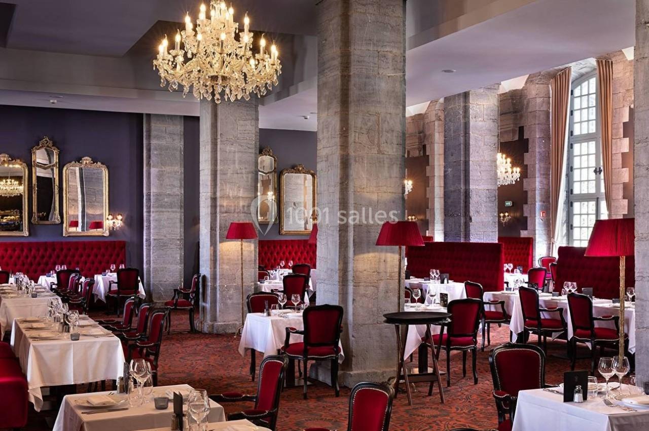 Salle de restaurant élégante avec tables dressées, chaises rouges, lustres en cristal et murs ornés de miroirs.