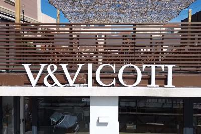Façade d'un bâtiment avec une enseigne ’V&VICOTI’ en lettres blanches, terrasse en bois et mobilier visible en arrière-plan.
