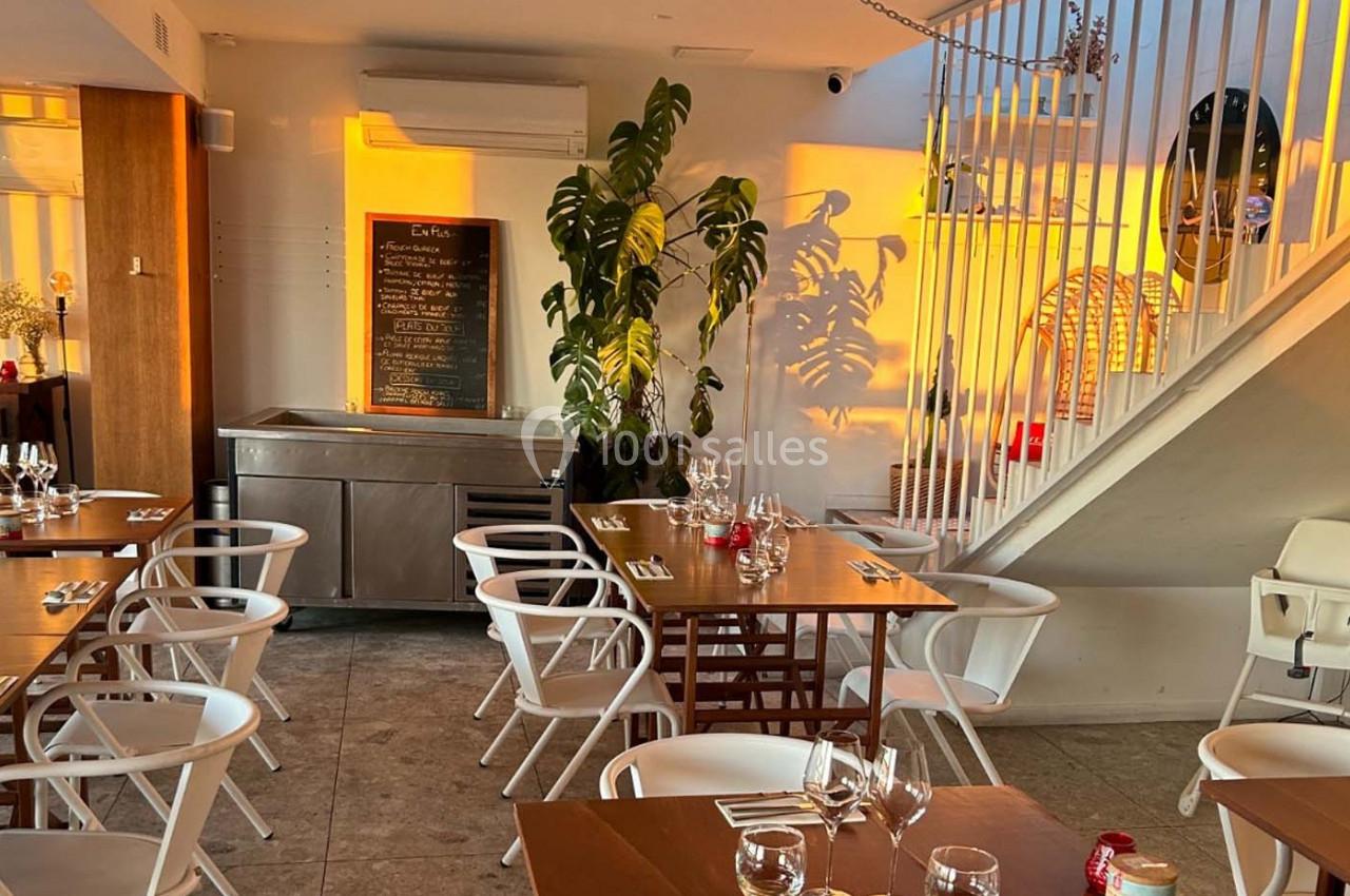 Salle de restaurant lumineuse avec tables dressées, plantes décoratives et tableau noir affichant le menu.