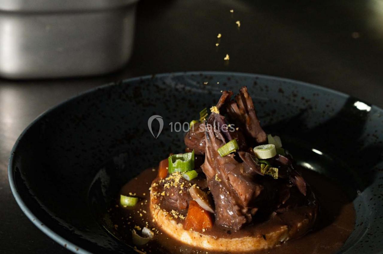 Plat de viande mijotée servie sur une tranche de pain, accompagnée de légumes et garnie d'oignons verts.