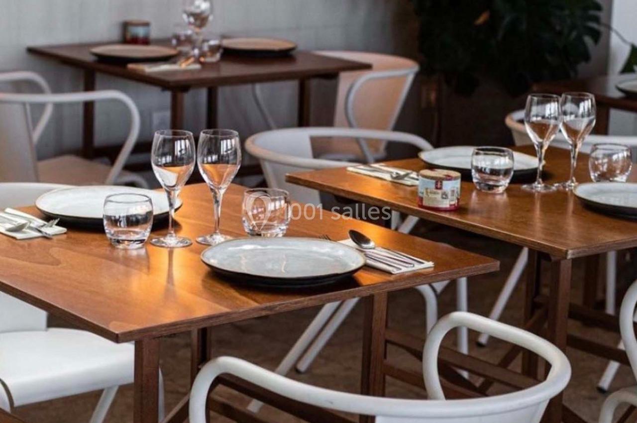 Tables en bois dressées avec assiettes, verres et couverts dans un restaurant, ambiance lumineuse et épurée.
