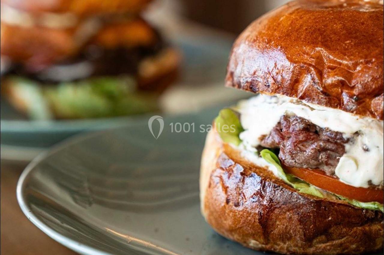Burger avec steak, laitue, tomate et sauce, servi dans un pain brioché sur une assiette grise.
