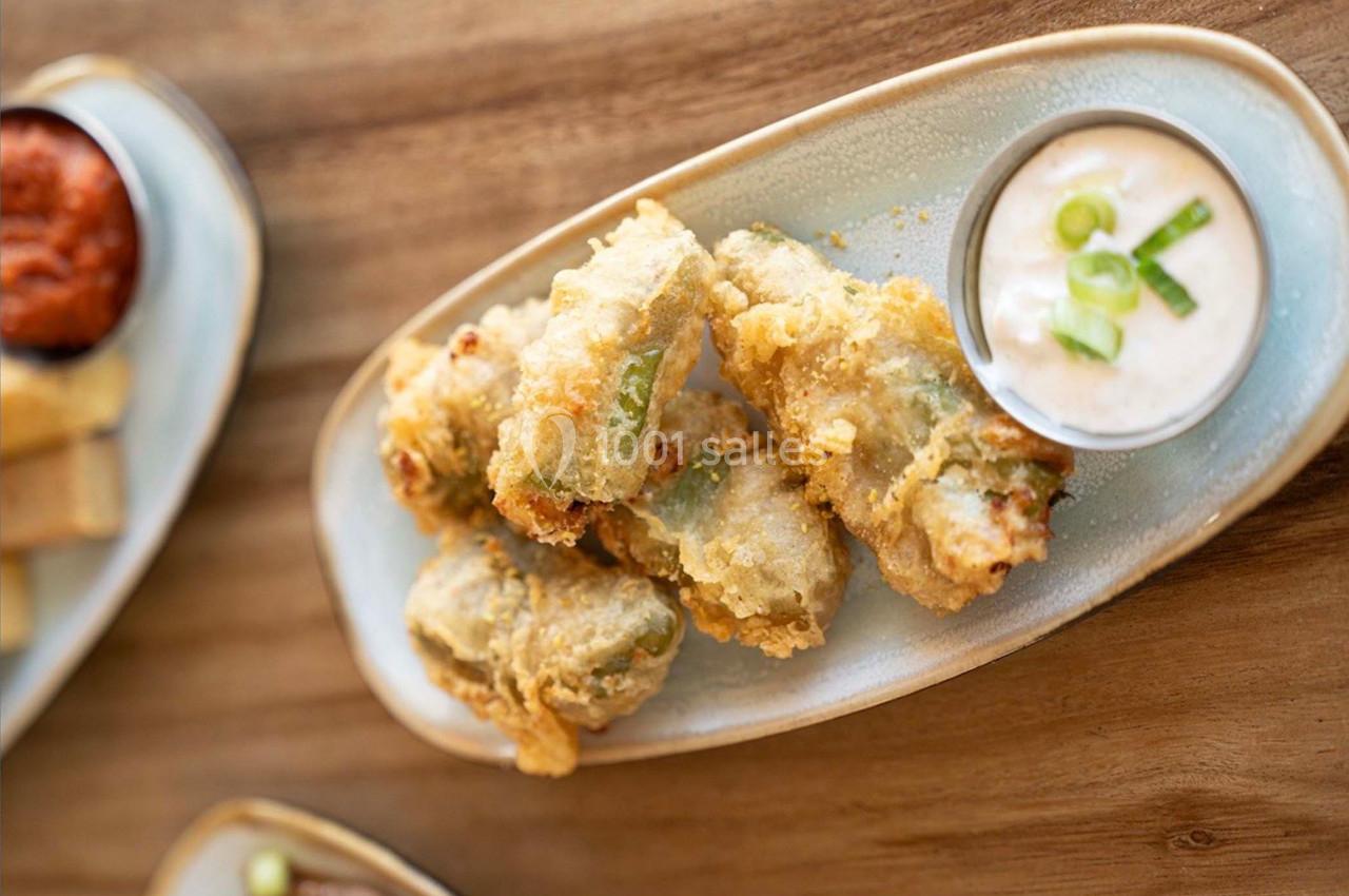 Assiette de beignets dorés accompagnés d'une sauce blanche garnie de ciboulette, sur une table en bois.