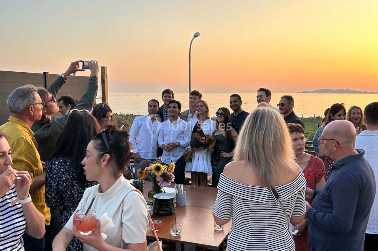 Groupe de personnes réunies en extérieur au coucher du soleil, certaines posant pour une photo, ambiance conviviale.