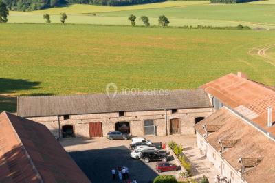 Vue aérienne d'une ferme en pierre entourée de champs verdoyants, avec des personnes rassemblées dans la cour.