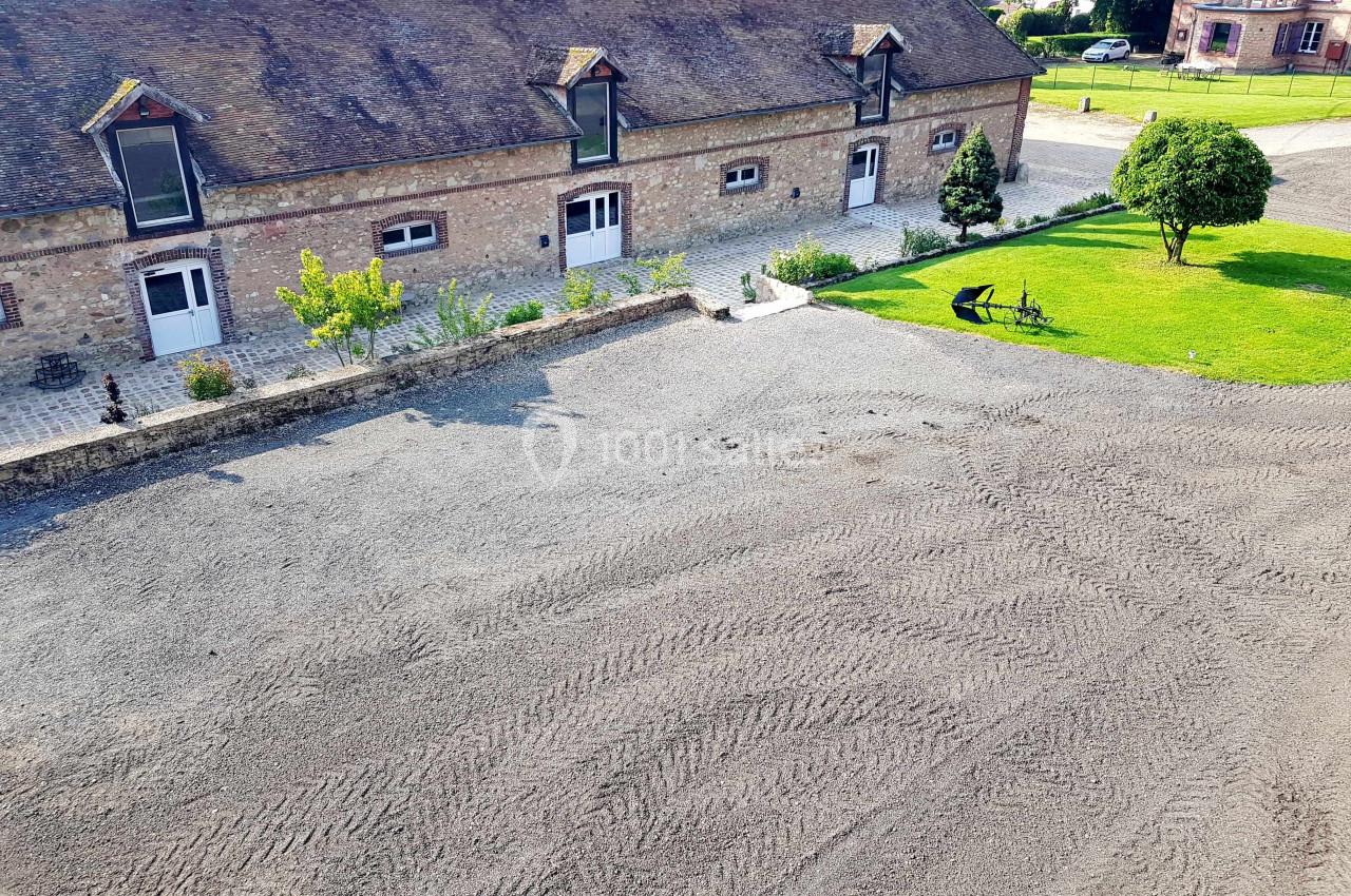 Cour d'une propriété avec bâtiment en briques, fenêtres mansardées, pelouse et allée en gravier.