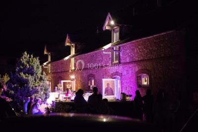 Vue aérienne d'une ferme en pierre entourée de champs verdoyants, avec des personnes rassemblées dans la cour.