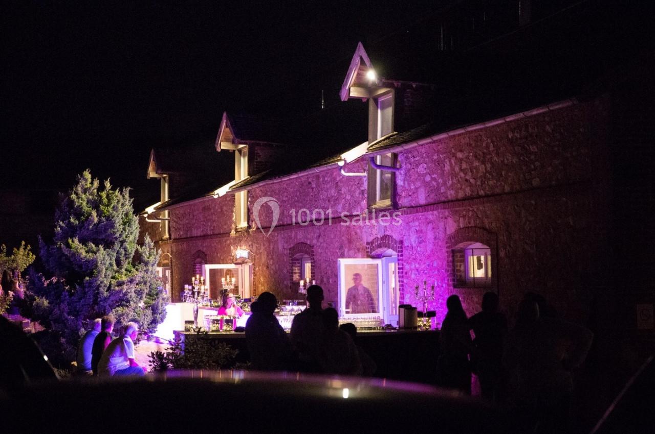 Façade en pierre éclairée par des lumières violettes, avec des silhouettes de personnes rassemblées devant.