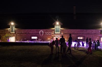 Vue aérienne d'une ferme en pierre entourée de champs verdoyants, avec des personnes rassemblées dans la cour.