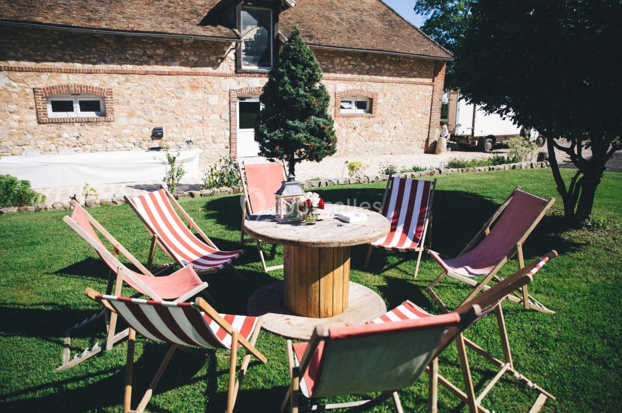 Chaises longues disposées en cercle autour d'une table en bois dans un jardin devant une maison en pierre.
