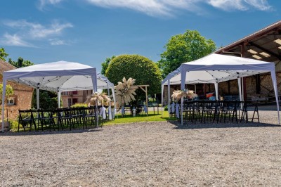 Vue aérienne d'une ferme en pierre entourée de champs verdoyants, avec des personnes rassemblées dans la cour.