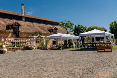 Vue aérienne d'une ferme en pierre entourée de champs verdoyants, avec des personnes rassemblées dans la cour.