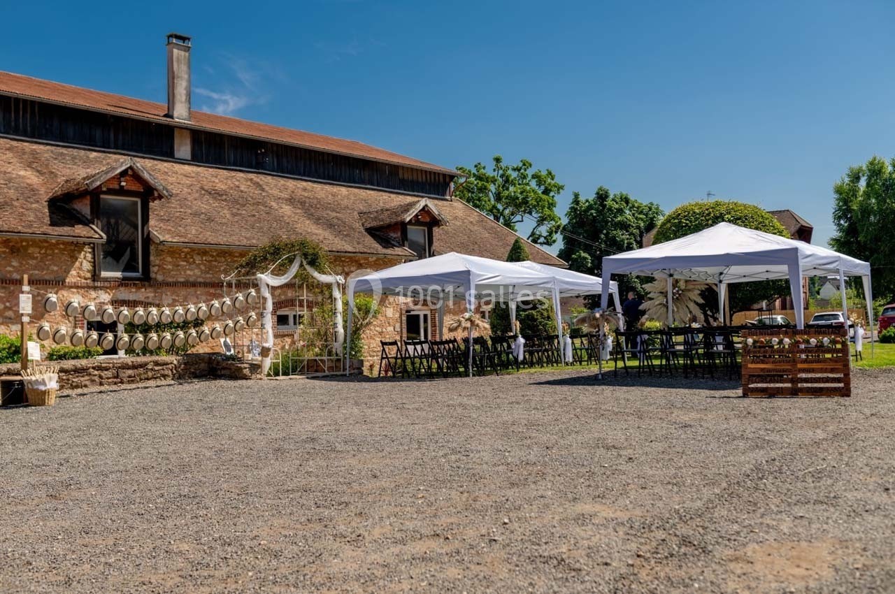 Cour extérieure d'une ferme avec des tentes blanches, des tables et des décorations pour un événement en plein air.