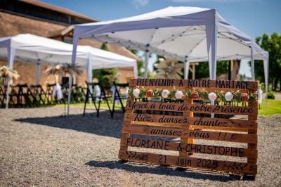 Vue aérienne d'une ferme en pierre entourée de champs verdoyants, avec des personnes rassemblées dans la cour.