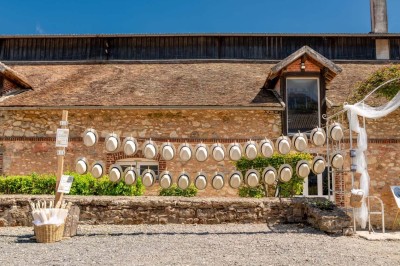 Vue aérienne d'une ferme en pierre entourée de champs verdoyants, avec des personnes rassemblées dans la cour.