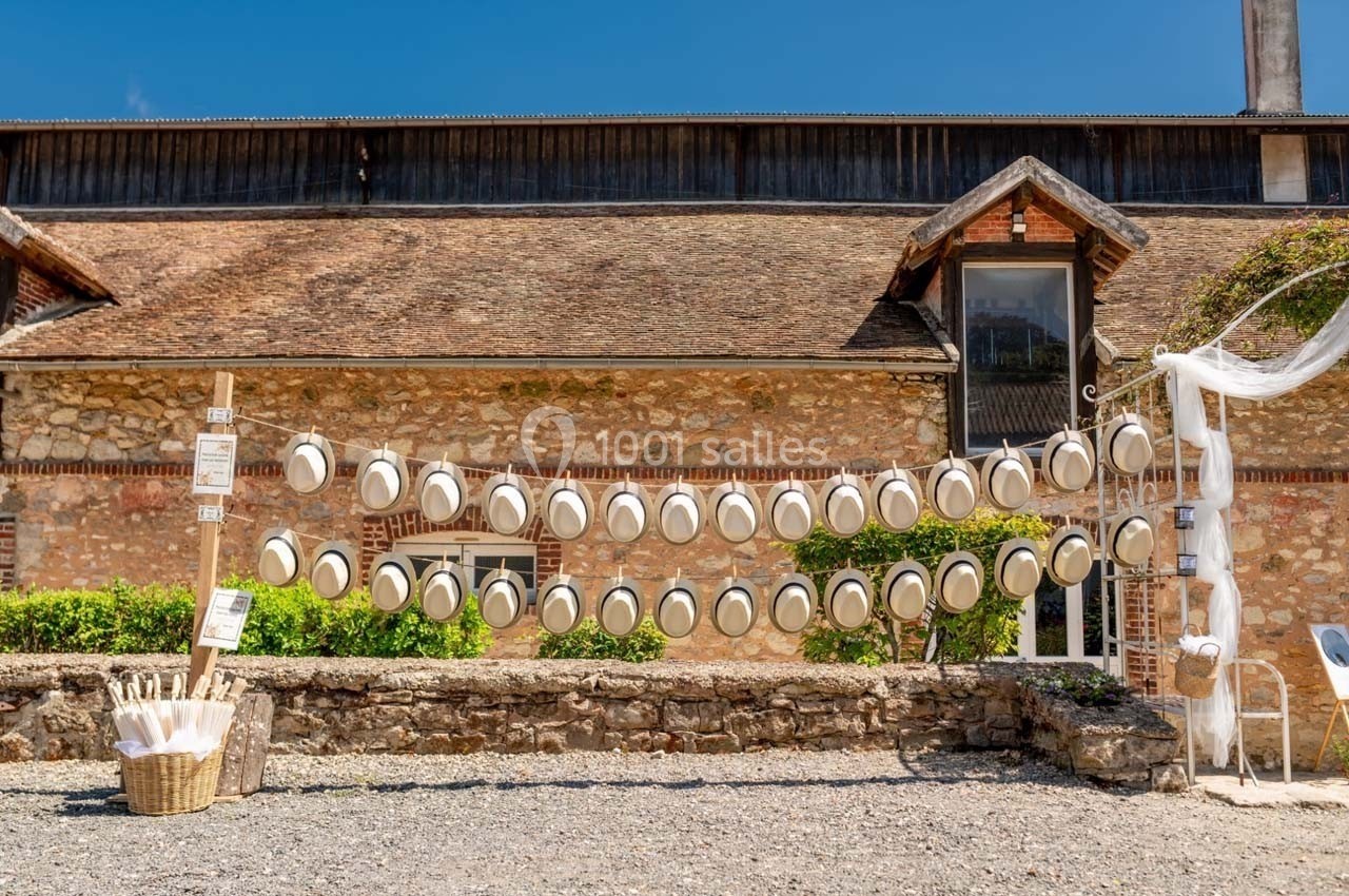 Chapeaux blancs suspendus sur des cordes devant un mur en pierre, avec un panier d'accessoires à gauche.