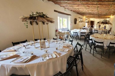 Vue aérienne d'une ferme en pierre entourée de champs verdoyants, avec des personnes rassemblées dans la cour.