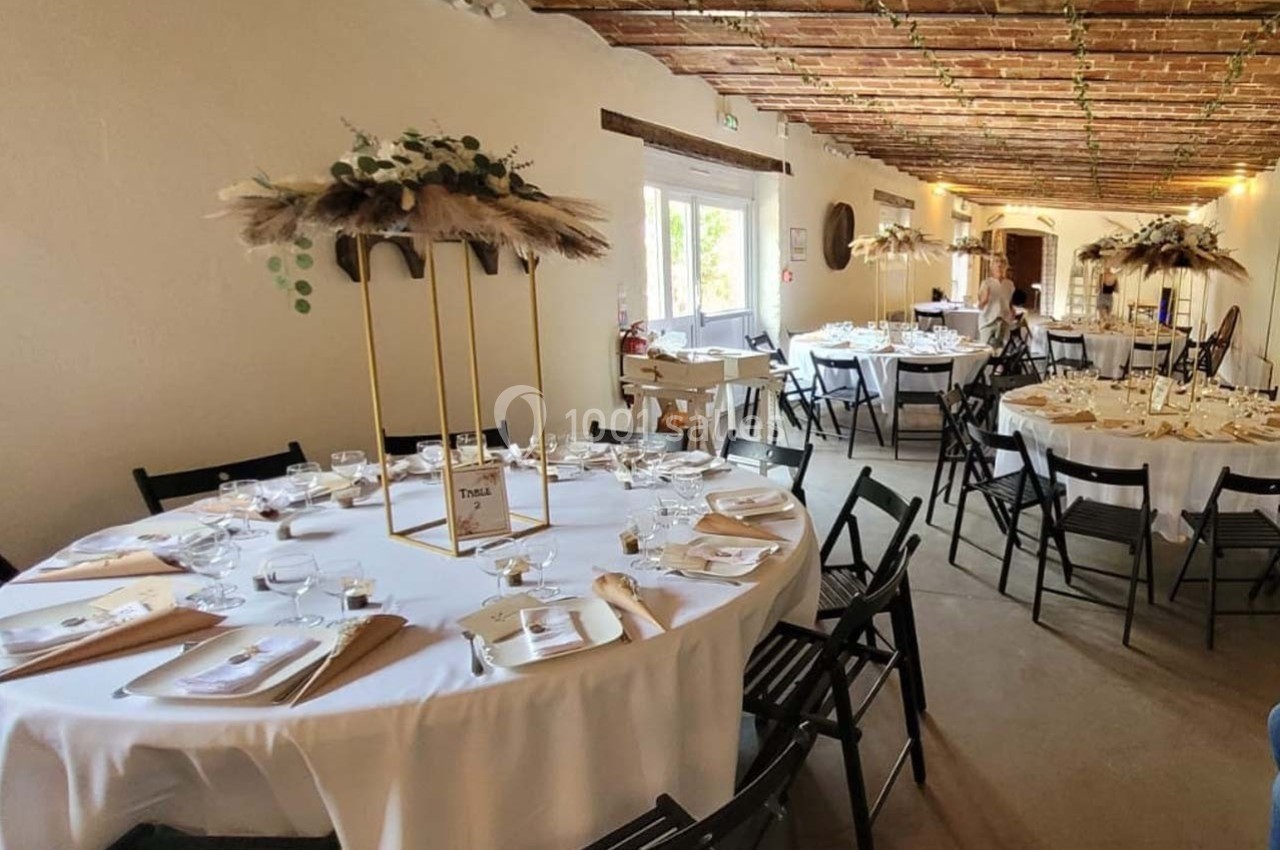 Salle de réception décorée avec des tables rondes dressées, nappes blanches et centres de table floraux.