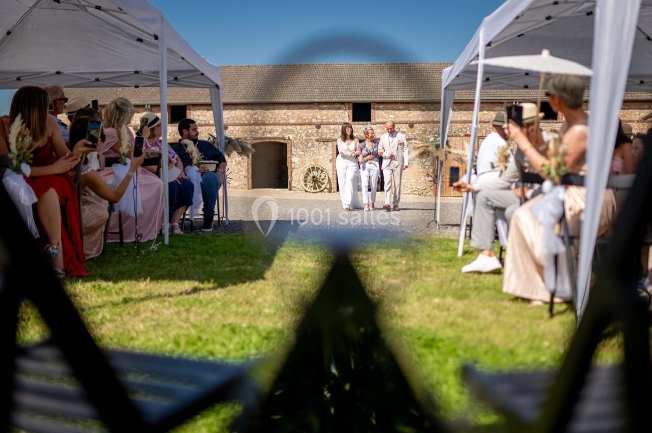 Cérémonie de mariage en extérieur sous des tentes blanches, avec des invités assis et un couple marchant au centre.