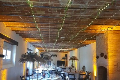 Vue aérienne d'une ferme en pierre entourée de champs verdoyants, avec des personnes rassemblées dans la cour.