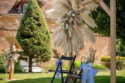 Vue aérienne d'une ferme en pierre entourée de champs verdoyants, avec des personnes rassemblées dans la cour.