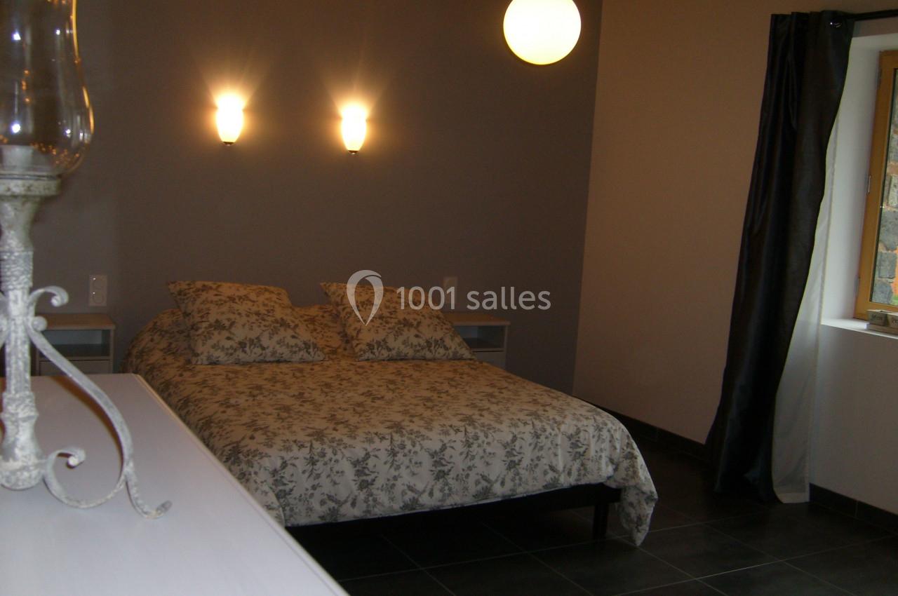 Chambre avec un lit double, éclairage mural, lampe suspendue, rideaux sombres et mur peint en gris.