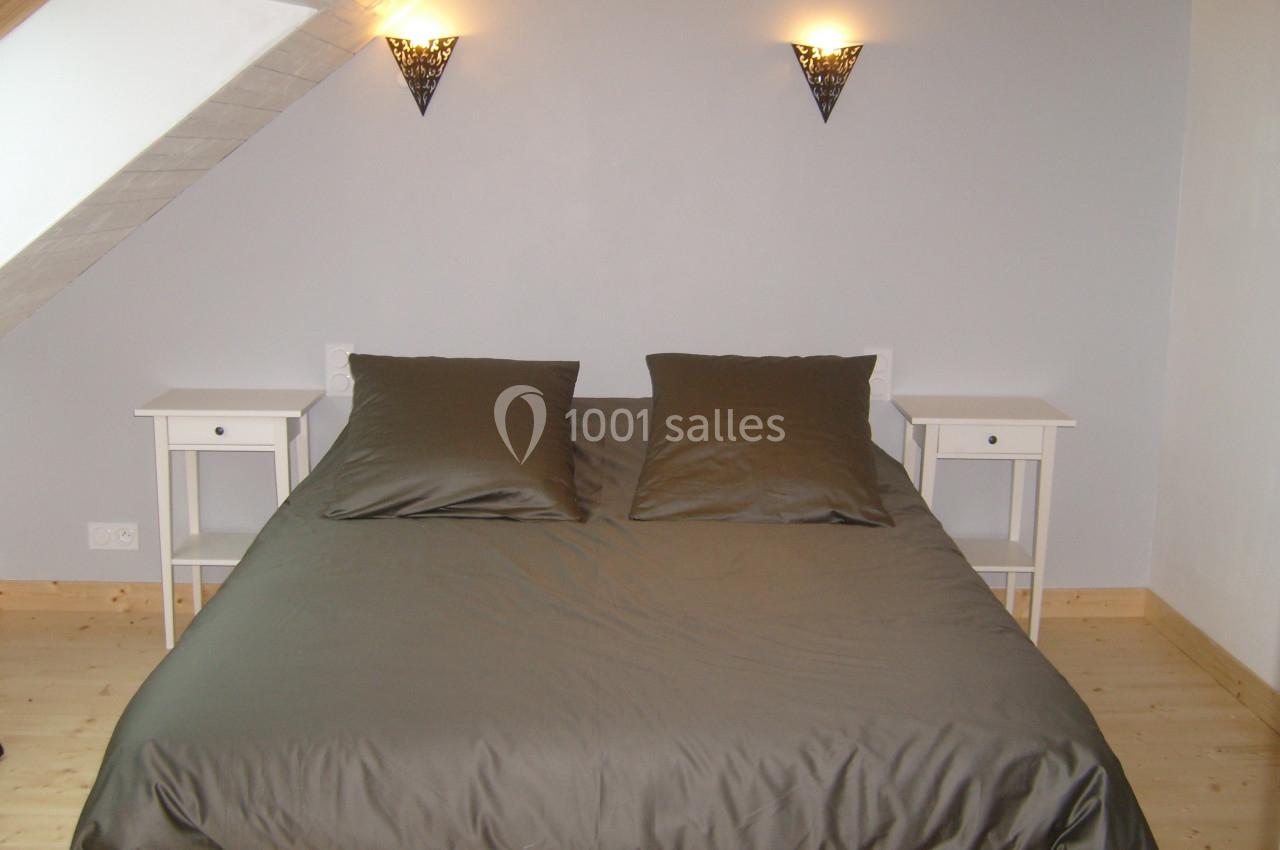 Lit double avec draps gris foncé, encadré par deux tables de chevet blanches et éclairé par deux appliques murales.