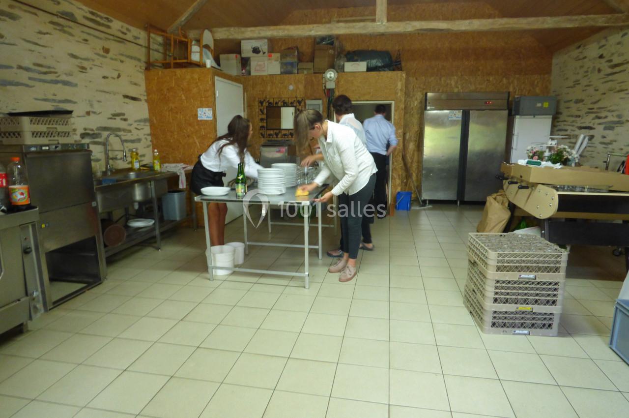 Des personnes préparent et rangent de la vaisselle dans une cuisine spacieuse avec des équipements professionnels.