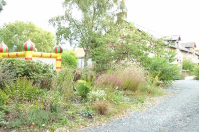 Allée bordée de végétation dense avec un château gonflable coloré visible à gauche et des bâtiments en arrière-plan.