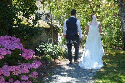 Allée bordée de végétation dense avec un château gonflable coloré visible à gauche et des bâtiments en arrière-plan.