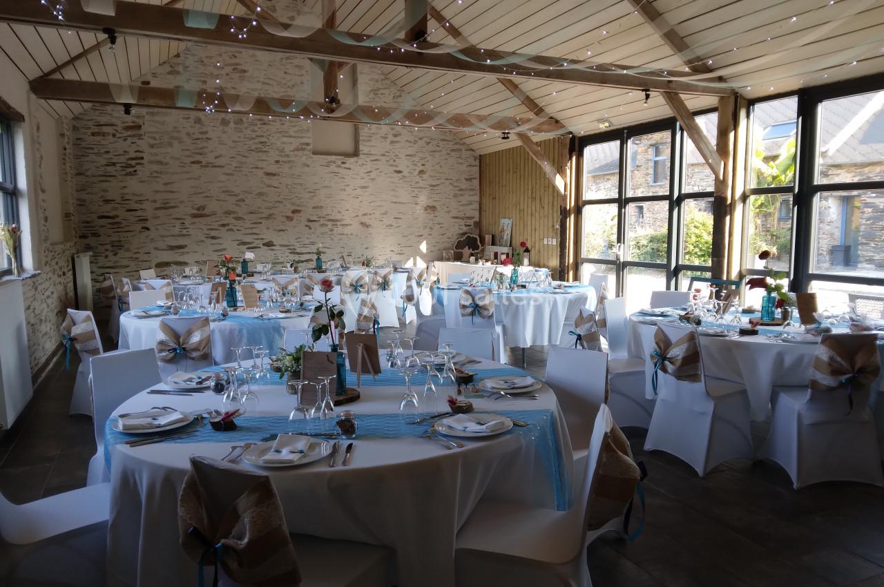 Salle de réception décorée pour un événement, avec des tables rondes dressées, nappes blanches et touches de bleu.