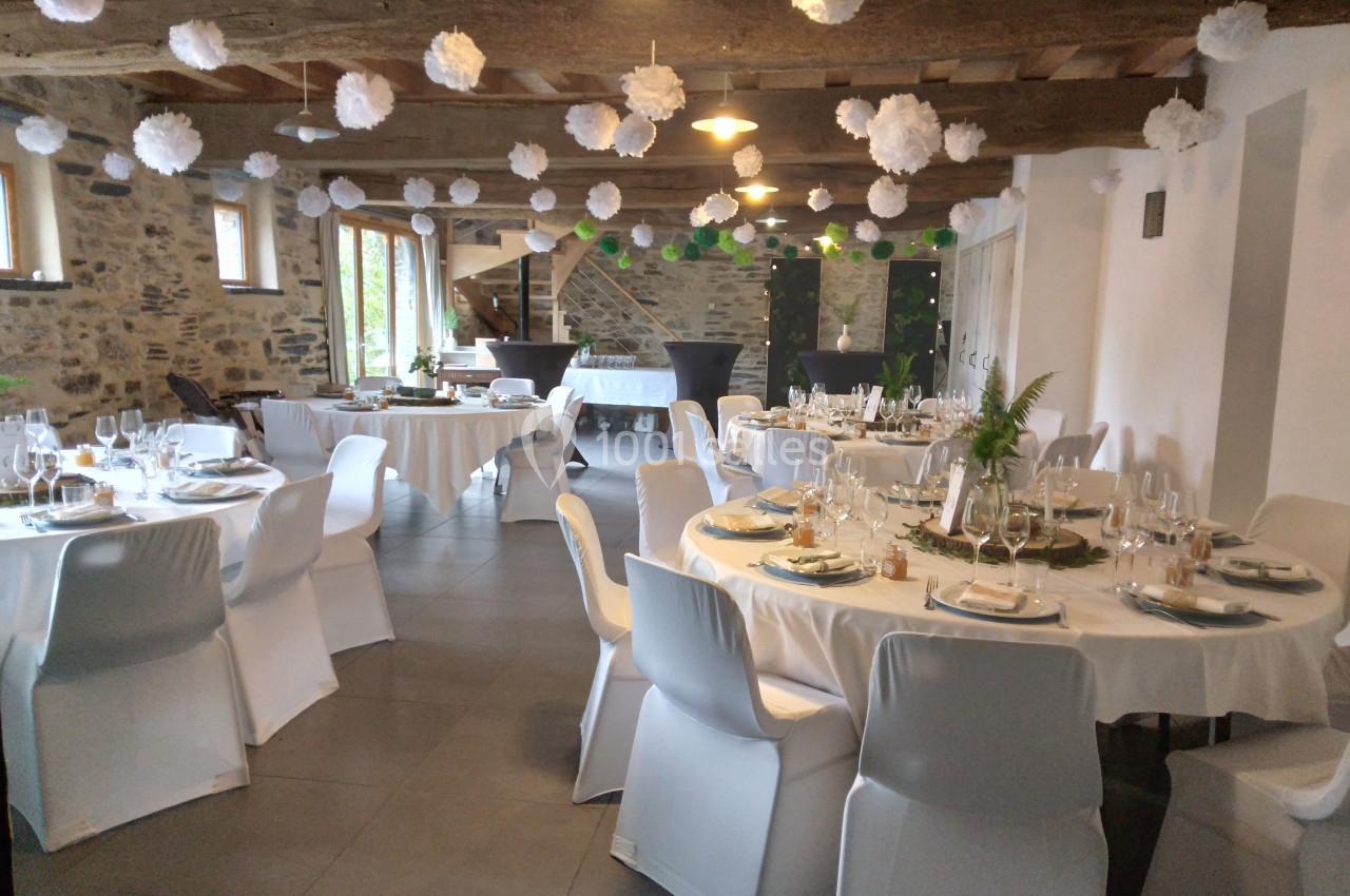 Salle de réception décorée avec des tables rondes dressées, des chaises blanches et des suspensions en papier.
