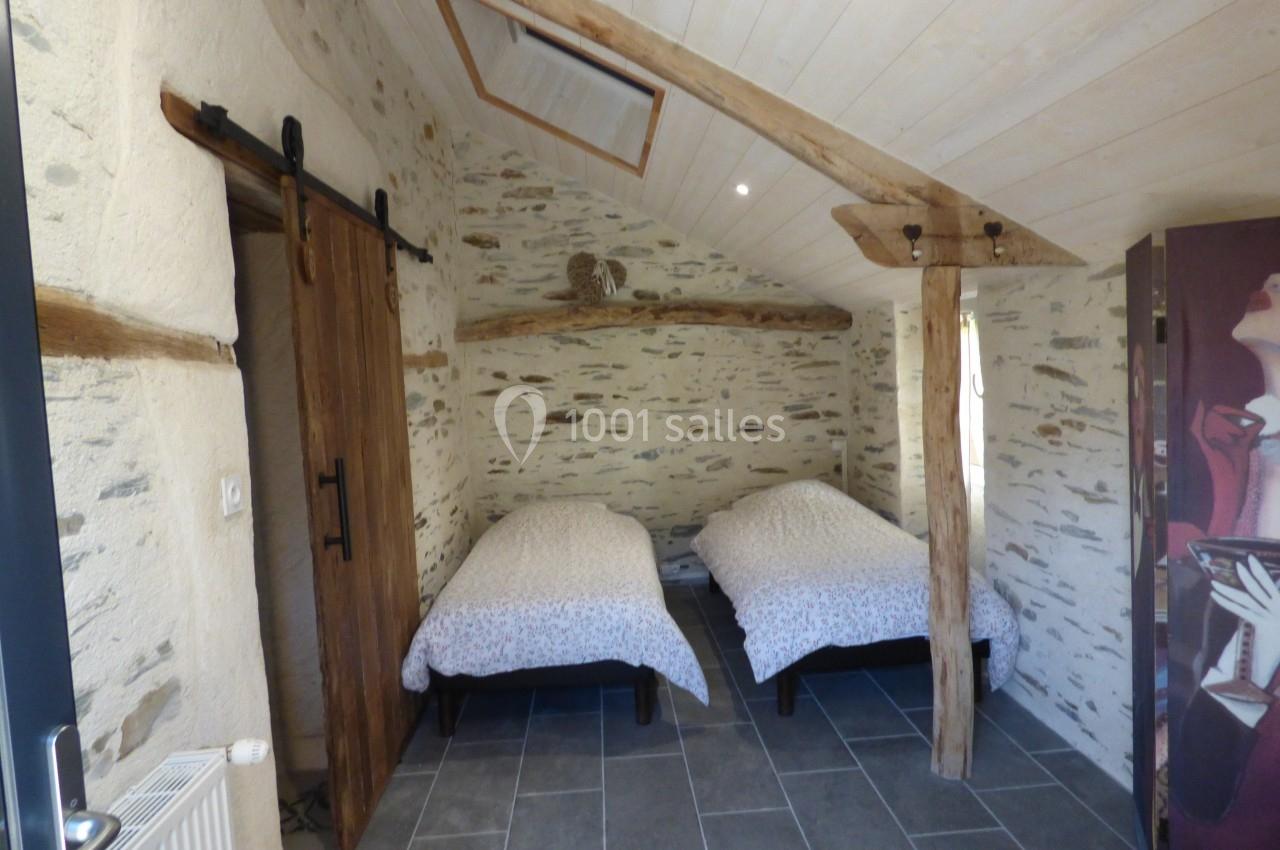 Deux lits simples dans une chambre rustique avec murs en pierre, poutres apparentes et porte coulissante en bois.